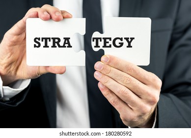 Close up of the hands of a businessman holding two pieces of a puzzle with the word Strategy split across them conceptual of forward thinking, planning and problem solving.
