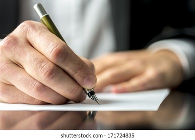Close up of the hands of a businessman in a suit signing or writing a document on a sheet of white paper using a nibbed fountain pen