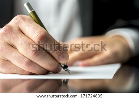 Close up of the hands of a businessman in a suit signing or writing a document on a sheet of white paper using a nibbed fountain pen