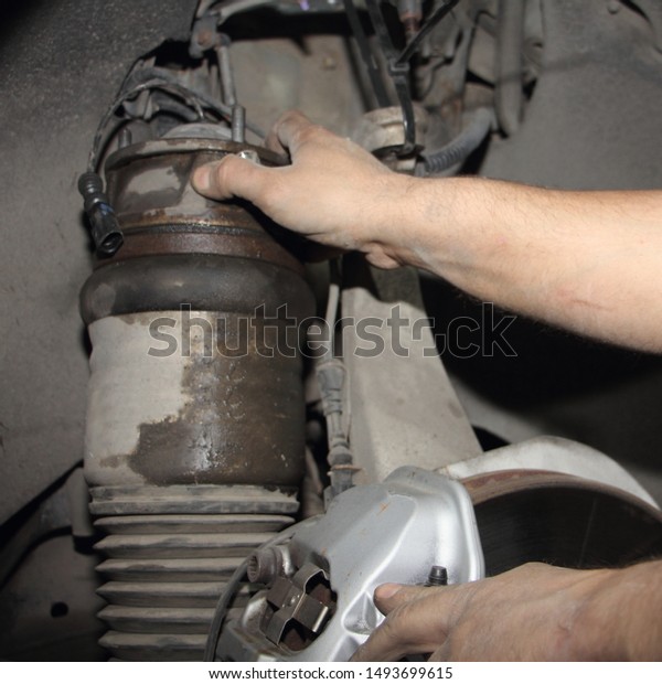 Close\
up hands of car mechanic fitting the pneumatic cylinder of front\
suspension rack, repair the air spring of the\
car