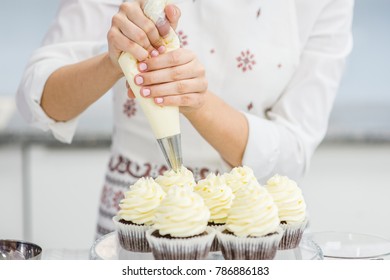 Close Up Hands Of The Chef With Confectionery Bag Squeezing  Cream On Cupcakes