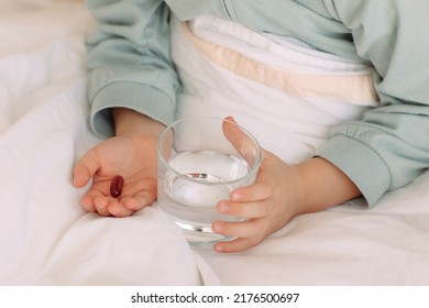 Close Up Hands Child In Bed Holds Pill And Glass Of Water Taking Medicine, Vitamin Mineral Supplements,nutrition,health Care, Treatment