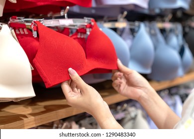Close up of hands choosing bras cups size and looking light new wireless and seamless technology with red hot color and sexy bra in lingerie shop at department store. Woman shopping underwear concept.