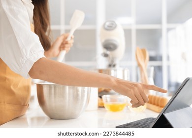 Close up of hands with computer in kitchen.Learn cooking online. A young woman is watching cooking tutorial video in the kitchen.Reading recipe while making cookies Following Recipe On Digital Tablet. - Shutterstock ID 2273844485