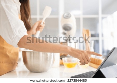Close up of hands with computer in kitchen.Learn cooking online. A young woman is watching cooking tutorial video in the kitchen.Reading recipe while making cookies Following Recipe On Digital Tablet.