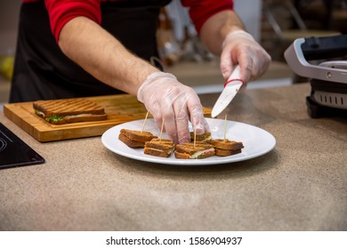 close up of hands of a cook man in rubber gloves put on a white plate snacks grilled sandwiches. soft focus, background is kitchen in blur - Shutterstock ID 1586904937