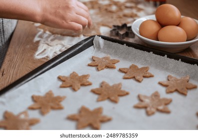 Close up of hands cutting christmas cookies with cookie cutters and arranging them on baking tray - Powered by Shutterstock