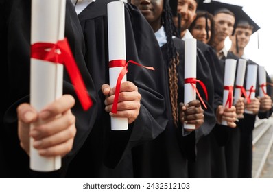 Close up hands of diverse graduate students holding diplomas and standing in a row in black robes outdoor at graduation ceremony. Education and graduating from university or college concept. - Powered by Shutterstock