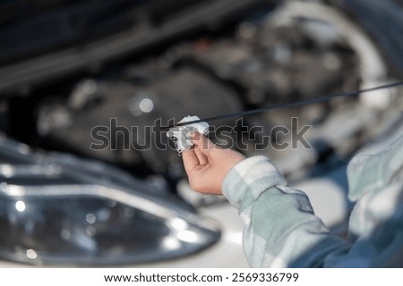 Close up of hands of female driver checking oil level in car engine. 