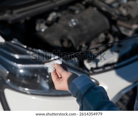 Close up of hands of female driver checking oil level in car engine. 