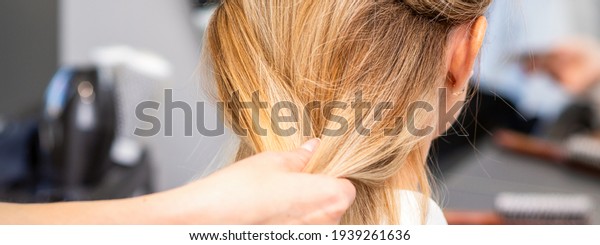 Close up of hands of female hairdresser\
styling hair of a blonde woman in a hair\
salon