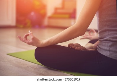 Close up hands. Girl do yoga indoors. Woman exercising yoga at sunset with a warmth background in gym. Young woman conducts meditating indoors.