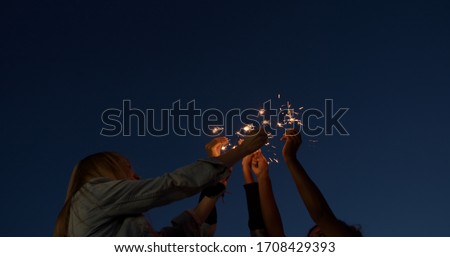 close up of hands of girls holding sparklers . Group of friends celebrating waving sparkler fireworks dancing enjoying party having fun holiday celebration at evening social gathering on rooftop