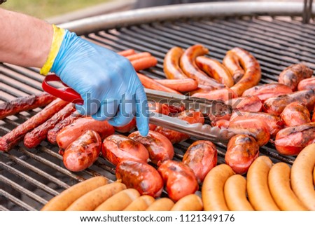 Close up of hands grilling sausages on bbq on warm summer day