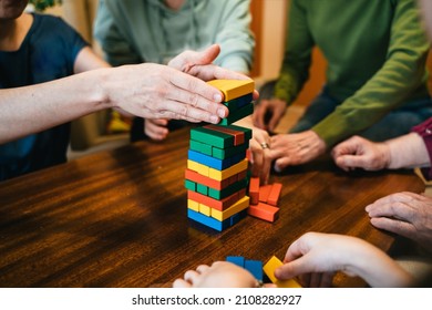 Close up of hands helping build a building of wooden pieces. Family playing game. Close-up view of woman and girls hand taking a piece from a tower.