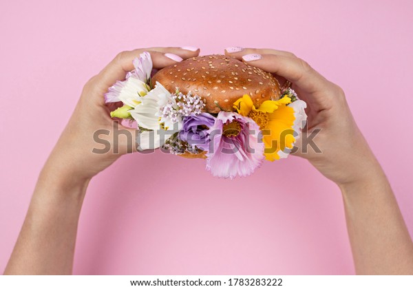Close Up of hands holding burger filled with\
flowers on pink\
background