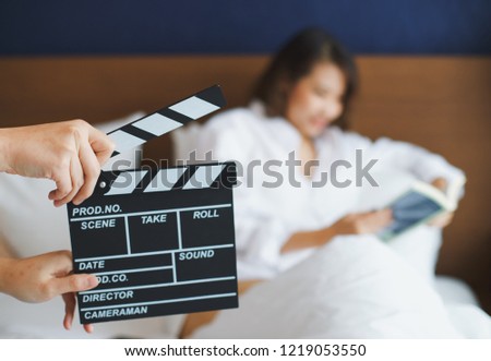 Close up hands holding clapperboard during the production of the film with asian woman reading a book in the scene 