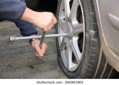 Close Up Of Hands Holding Cross Wrench To Remove Flat Tire Of Stranded Car