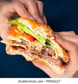 Close up of hands holding hamburger, over dark blue background.