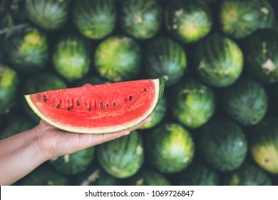 Close up hands holding piece of fresh red slice watermelon on the heap background