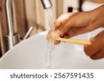 Close up of hands holding toothbrush under running tap water, preparing for oral hygiene routine in modern bathroom