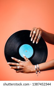 Close Up Of Hands Holding A Vinyl Record Against A Copper Orange Background. African American Woman Holding In Her Hands A Blank Vintage Record In Studio.