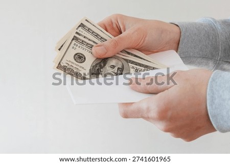 Close up of hands holding a white envelope containing US dollar banknotes. Cash money partially visible inside the envelope. Isolated on white background.