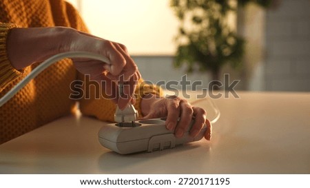 Close up of hands inserting a power plug into a surge protector on a table, with a blurred background.