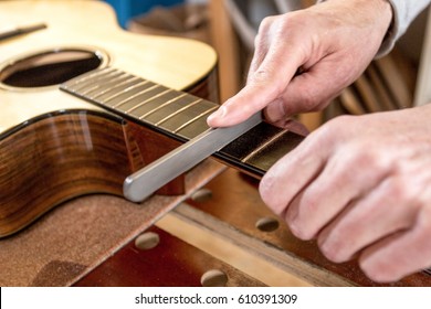 Close up of the hands of an instrument maker, filing the frets of an acoustic guitar - Shutterstock ID 610391309
