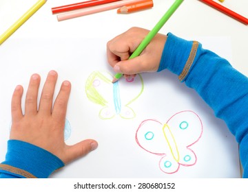 Close up of the hands of a little child drawing a butterfly with color pencils