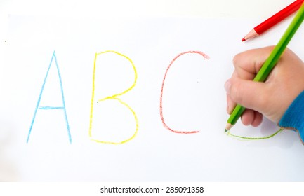 Close Up Of The Hands Of A Little Child Writing Letters With Color Pencils