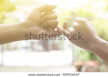 close up hands of lovely couple hooking each other's little finger together with copy space for text and soft light effect: pinky swear, pinkie promise concept