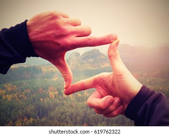 Close up  hands make frame gesture. Melancholy misty valley bellow rocky peak. Cold spring daybreak in mountains. Have a fun