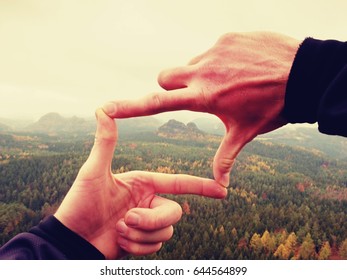 Close up  hands make frame gesture. Melancholy misty valley bellow rocky peak. Cold spring daybreak in mountains.