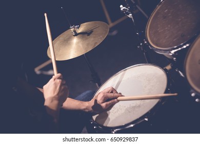 Close up of hands of male drummer holdning drumsticks sitting and playing drums in studio - Powered by Shutterstock