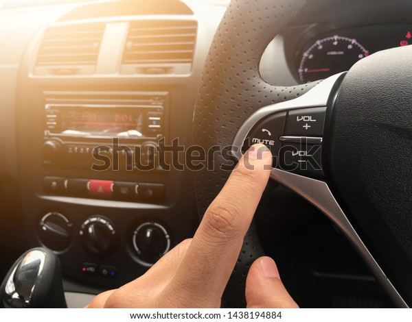 Close up of the hands of a man\
driver with finger point at mute button for not receiving phone\
calls while driving concept. Light leak effect in the\
evening.