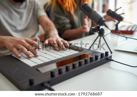Close up of hands of man making music using equipment, drum pad machine. Female and male bloggers recording video blog or vlog at home. Blogging, music, creation. Focus on drum pad and hand