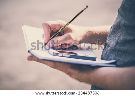 close up hands man writing on diary and smartphone outdoor