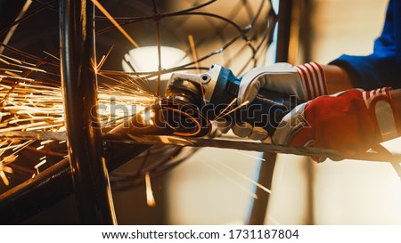 Close Up of Hands of a Metal Fabricator Wearing Safety Gloves and Grinding a Steel Tube Sculpture with an Angle Grinder in a Studio. Working with a Handheld Power Tool in a Workshop.