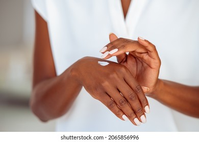 Close up hands of middle aged black woman applying cream to moisturize them. African american woman rubbing white moisturizer on hands. Woman testing nourishing body lotion on the back of the hand. - Powered by Shutterstock