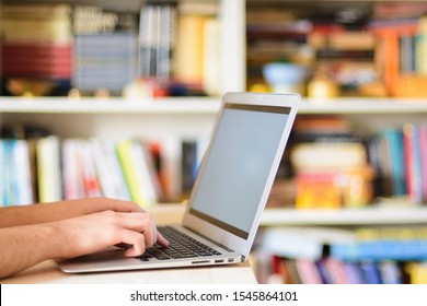 Close up hands multitasking man using notebook computer in library, room full of books studying