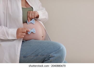 Close Up Hands On Pregnant Mother Holding Baby Clothes, Two Blue Bows. Lover Woman Waiting Child. Preparation For Childbirth, Girl Big Belly Advanced Pregnancy. Selective Focus