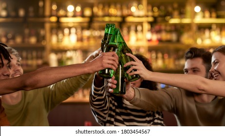 Close up of hands of people in the bar clinking bottles while drinking beer together. People, leisure, friendship and entertainment concept. Focus on hands and bottles. Side view. Web Banner - Powered by Shutterstock