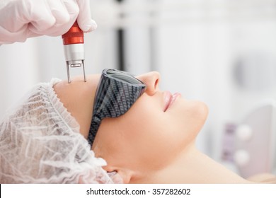 Close up of hands of professional beautician making skin treatment for woman. The lady is smiling with relaxation. She is lying and wearing goggles - Shutterstock ID 357282602
