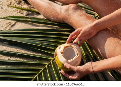close up of hands of sexy skinny woman in white bikini swimwear holding coconut drink, hips, sitting on tropical beach. slim body, sand on skin, vacation in Thailand, natural beauty, sunny summer