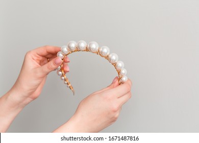 Close Up Of Hands Showing A Trendy Bridal Gold Diadem (hair Hood, Hair Band, Tiara) With Big Pearls. Wedding Accessories. Copy Space. Gray Background.