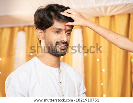 Close up Hands of Sister applying Tilak or mark to forehead of elder Brother during Bhai Dooj or Bhaubeej Indian religious festival.