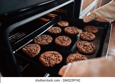 Close up of hands taking out a baking sheet from the oven with cookies with chocolate. Baking process concept - Powered by Shutterstock