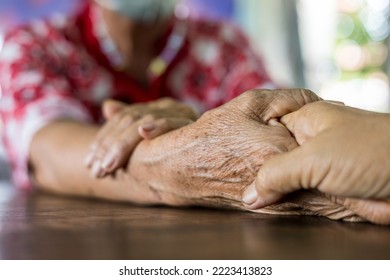 Close Up Hands Of Two Elderly Thai Women Sitting And Holding Hands Together On The Floor Of A Wooden Table To Comfort And Encourage Each Other On The Side Of The House.