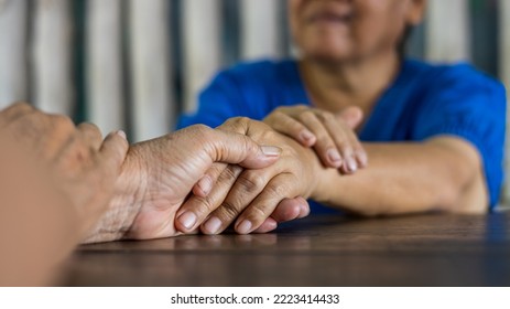 Close Up Hands Of Two Elderly Thai Women Sitting And Holding Hands Together On The Floor Of A Wooden Table To Comfort And Encourage Each Other On The Side Of The House.